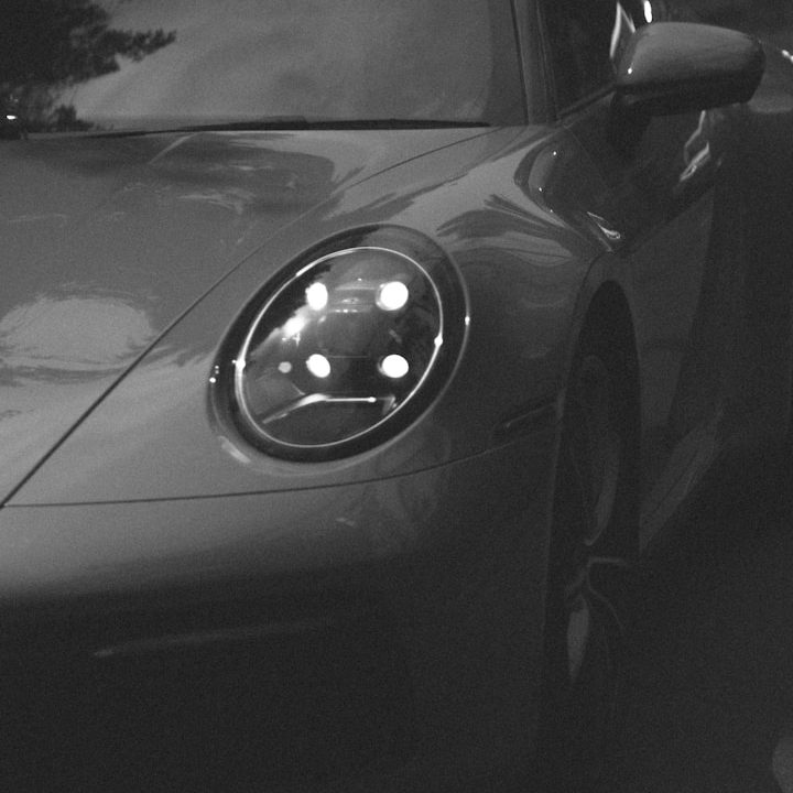 Nahaufnahme eines grauen Porsche Sportwagens mit leuchtenden Scheinwerfern.